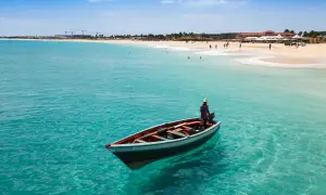 Ein Mann in einem Boot auf dem türkisfarbenen Meer vor Kapverden. Die Flugzeit dorthin lohnt sich für diesen Anblick.