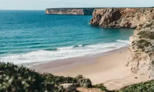 Traumhafter Strand mit Klippen und türkisfarbenem Meer. Perfekt für einen Portugal Urlaub mit Surfern im Wasser.