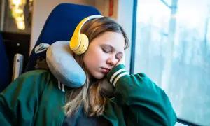 Mädchen schläft im Zug mit gelben Kopfhörern und einem Nackenkissen richtig benutzt für bequemen Halt.