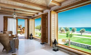 Ein luxuriöses Zimmer mit Meerblick im Mitsis Blue Domes. Eine Frau steht auf dem Balkon und genießt die Aussicht.
