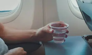 Hand hält ein Glas Wasser, während man im Flugzeug sitzt.