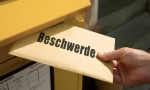 Ein Brief mit der Aufschrift "Beschwerde" wird in einen gelben Briefkasten eingeworfen. Vielleicht eine TUI Reklamation?