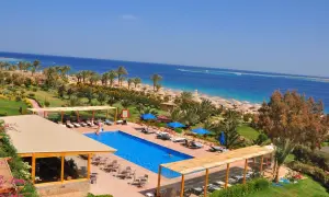 Ein luxuriöser Poolbereich mit Blick auf das Meer und den Strand des Fort Arabesque West Bay. Palmen und Sonnenschirme säumen den Weg zum türkisfarbenen Wasser.