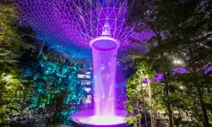 Imposanter Wasserfall im Jewel Changi Airport Singapur, beleuchtet in lila und blau unter einem geometrischen Glasdach.