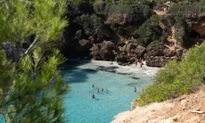 Türkisblaues Wasser in einer malerischen Bucht auf Mallorca. Menschen sonnen sich auf Felsen und schwimmen im Meer.