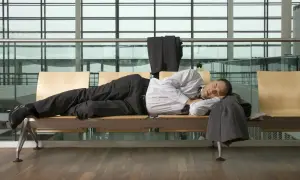 Mann schläft am flughafen auf einer Bank, sein Anzug hängt über der Lehne.