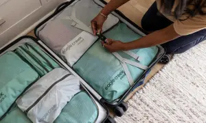 Frauen packen ihre Koffer mit praktischen Reise-Must-Haves: Packwürfel in Mintgrün und Grau sortieren Kleidung für die nächste Reise.
