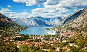 Traumhafter Urlaub in Montenegro: Die Bucht von Kotor mit Kreuzfahrtschiff und malerischer Stadt vor imposanter Bergkulisse.