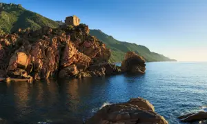 Ein alter Turm thront auf roten Felsen am Meer. Perfekt für einen Urlaub im Juli.