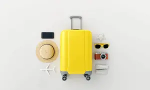 Gelbe Reisetasche mit Hut, Sonnenbrille, Kamera, Handy und Flugzeug – die perfekten roadtrip must haves für deinen Urlaub.