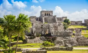 Ruinen von Tulum, ein Traumziel für jeden Mexiko Urlaub. Palmen und antike Bauten unter blauem Himmel.