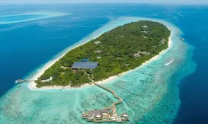 Soneva Fushi: üppige Insel mit Villen, Solaranlagen und einem Steg zu einem Restaurant im türkisfarbenen Wasser.