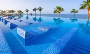 Infinity-Pool mit integrierten Liegen im Riu Gran Canaria, Palmen und Meer im Hintergrund.