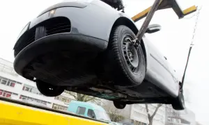 Ein graues Auto wird mit Gurten und Ketten von einem Abschleppwagen gehoben. Es muss wohl abgeschleppt werden.