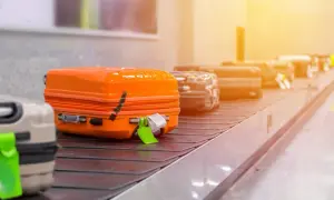 Koffer auf Gepäckband. Ein orangefarbener Koffer mit Klebeband und Anhänger. Hier beginnt die Geschichte, warum Koffer verloren gehen.