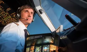Ein Pilot im Cockpit, der aufmerksam auf die Instrumente blickt. Er trägt Kopfhörer und eine Uniform, wie ein deadhead pilot, der auf seinen Einsatz wartet.