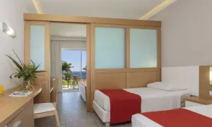 Zwei Betten mit roten Decken im Rodos Princess Beach Hotel. Ein Schreibtisch mit Blumen und Blick aufs Meer.
