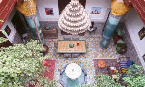 Ein Innenhof in Marrakesch mit Mosaikböden, einer Fontäne, üppiger Vegetation und einem Kronleuchter. Perfekt für einen entspannten Urlaub.