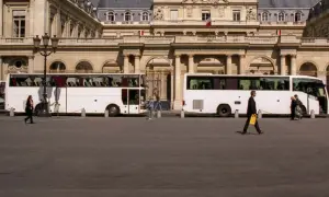 Weiße Reisebusse vor einem prächtigen Gebäude. Eine Frau geht vorbei. Wie kommt man am besten nach Paris? Mit dem Bus!