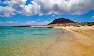 Traumhafter Strand mit türkisfarbenem Wasser und einem Vulkan im Hintergrund – ideal für Ihren Kanaren Urlaub.