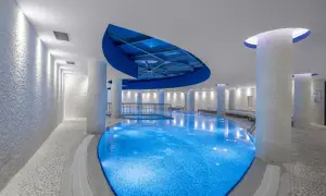 Ein luxuriöses Schwimmbad mit blau beleuchtetem Wasser, umgeben von weißen Säulen und Mosaikwänden. Ein Ort, der wie ein **rubi platinum sign** für Entspannung wirkt.