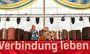 Zwei Frauen präsentieren eine Auswahl an Koffern für eine Auktion. Die Koffer sind in verschiedenen Farben und Mustern erhältlich.