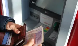 Person hält Geld und Portemonnaie vor Geldautomat. Hier kann man bei der Bank Geld wechseln.