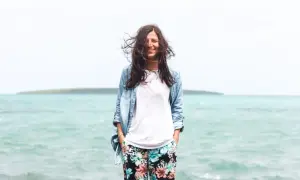 Frau mit wehendem Haar am Meer, die lächelt. Perfekt für die Packliste Mauritius: leichte Kleidung, Jeansjacke und bunte Hose.