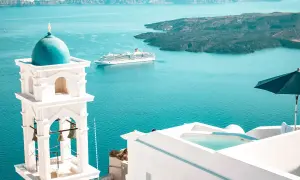 Traumhafter Urlaub Griechenland: Weißer Glockenturm mit blauer Kuppel, Kreuzfahrtschiff auf dem Meer, Infinity-Pool und Sonnenschirm.