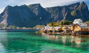 Idyllische Fischerhäuser auf Stelzen am kristallklaren Wasser vor majestätischen Bergen. Ein perfekter Urlaub in Norwegen.