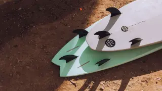 Zwei Surfbretter mit Finnen liegen auf sandigem Boden. Perfekt für die packliste surfcamp.