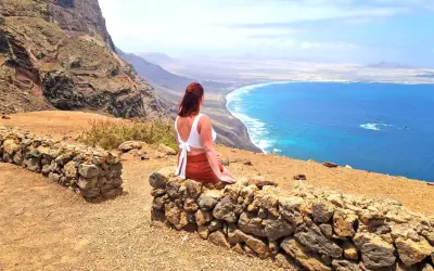 Frau genießt ihren Urlaub alleine auf einem Felsvorsprung mit Blick auf das türkisfarbene Meer und die Küste.