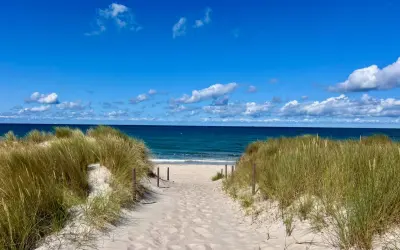 Sandiger Weg durch Dünen zum blauen Meer. Perfekter Urlaub am Meer mit Sonnenschein und Wolken.