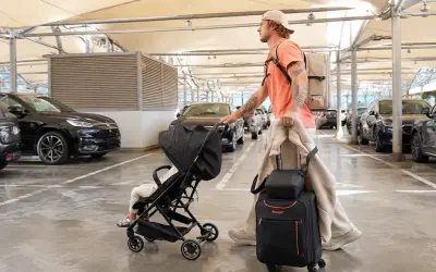 Mann mit Gepäck und Kinderwagen auf dem Parkplatz eines Flughafens.