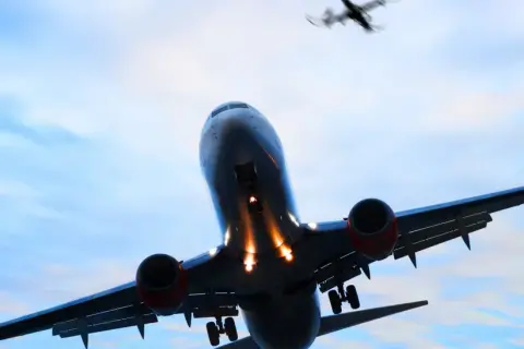 Ein landendes Flugzeug mit ausgefahrenem Fahrwerk im Gegenlicht, ein weiteres Flugzeug fliegt darüber.