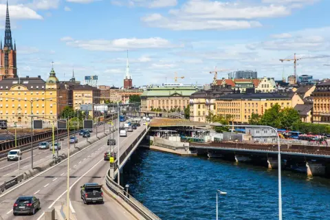 Blick auf die Skyline von Stockholm mit einem Fluss und einer Autobahn, auf der Autos fahren. Das Parken in Stockholm ist hier gut zu sehen.