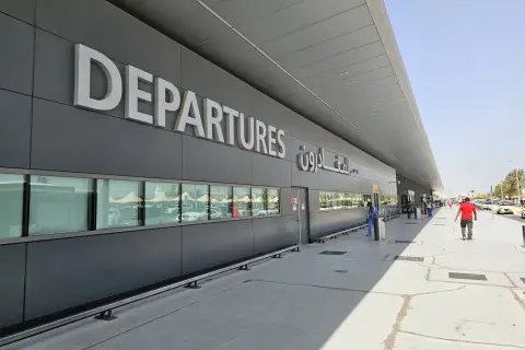 Große "DEPARTURES" Schriftzüge am Flughafen Dubai Terminal 3. Menschen und Autos spiegeln sich in den Fenstern.