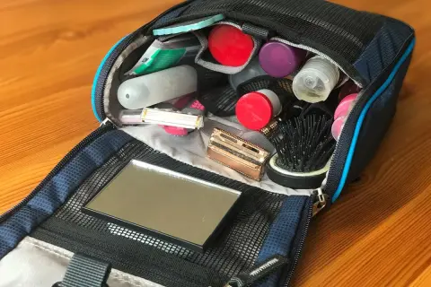 Offener Kulturbeutel mit Kosmetikartikeln: Zahnbürste, Rasierer, Kamm, Spiegel und diverse Fläschchen. Perfekte Packliste für unterwegs.