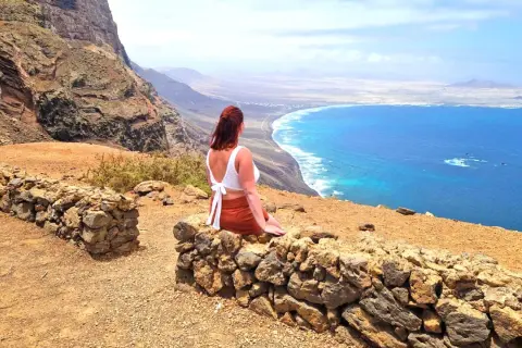 Frau genießt ihren Urlaub alleine auf einem Felsvorsprung mit Blick auf das türkisfarbene Meer und die Küste.