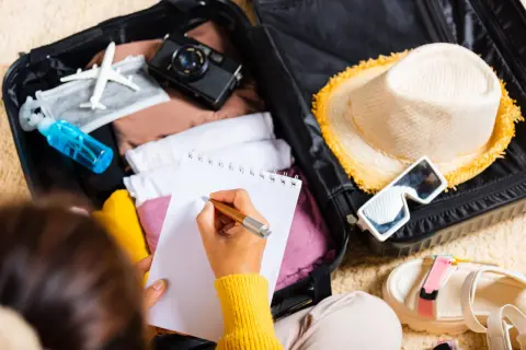 Packliste Portugal: Koffer packen mit Kleidung, Hut, Sonnenbrille, Kamera und Notizbuch.
