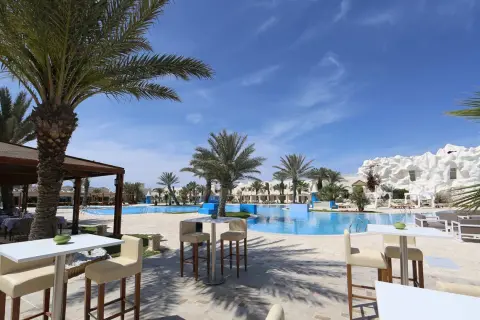 Sonnige Poolanlage mit Palmen und weißen Liegestühlen im Robinson Club Djerba.