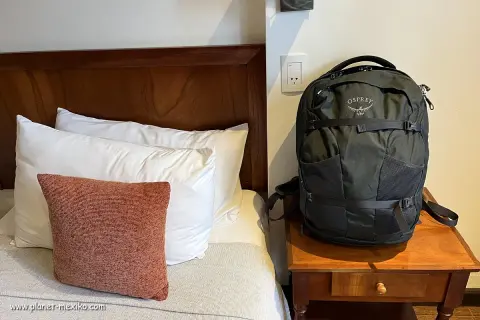Schwarzer Osprey-Rucksack neben einem Bett mit Kissen. Perfekt für deine Packliste Mexiko.