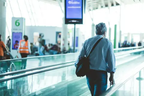 Mann mit Tasche auf Rolltreppe am Flughafen Frankfurt, auf dem Weg zum Geldwechsel.