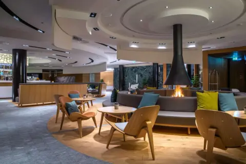 Gemütliche Lounge mit Kaminfeuer im Radisson Blu Hotel Andermatt. Moderne Sitzmöbel und Holzakzente laden zum Verweilen ein.