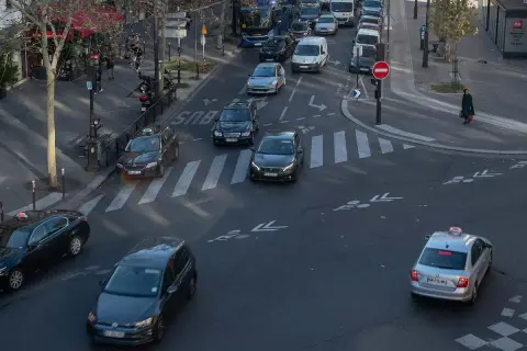 Verkehr in Paris: Autos und Taxis auf dem Weg zum Ziel. Ein silbernes Taxi fährt über den Zebrastreifen, während andere Fahrzeuge im Stau stehen.