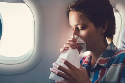 Frau mit Tüte gegen Reisekrankheit im Flugzeug.