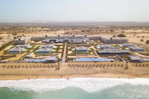 Luftaufnahme des Riu Palace Boavista Hotels mit mehreren Gebäuden, Pools und einem Strand mit Sonnenschirmen.