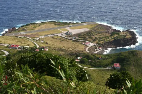 Ein Flugzeug landet auf der Landebahn des kleinsten Flughafens der Welt, umgeben von grünen Hügeln und dem blauen Meer.