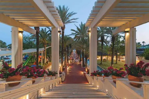 Ein beleuchteter Weg mit Palmen führt zum Seven Seas Hotel. Blumenkästen säumen die Treppe.