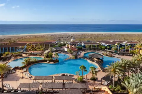 Ein Urlaubsparadies am Meer: Große Poollandschaft mit Palmen und Liegen, dahinter das Robinson Jandia Playa Resort und der weite Sandstrand.
